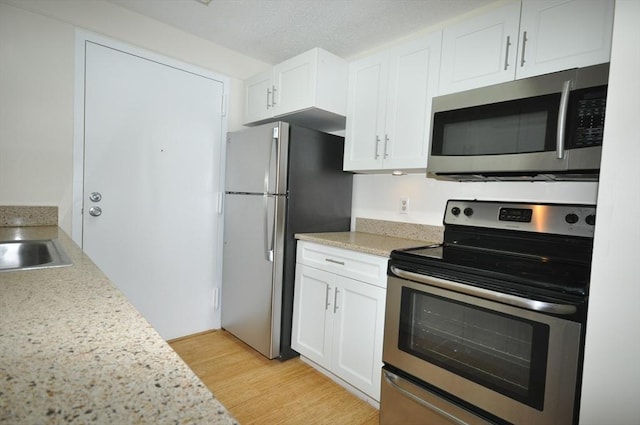 kitchen with appliances with stainless steel finishes, light wood-type flooring, and white cabinetry