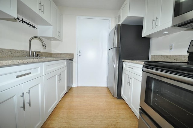 kitchen with white cabinets, light stone counters, a sink, light wood-style flooring, and stainless steel appliances