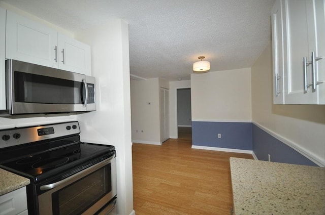kitchen featuring a textured ceiling, baseboards, white cabinets, light wood finished floors, and stainless steel appliances