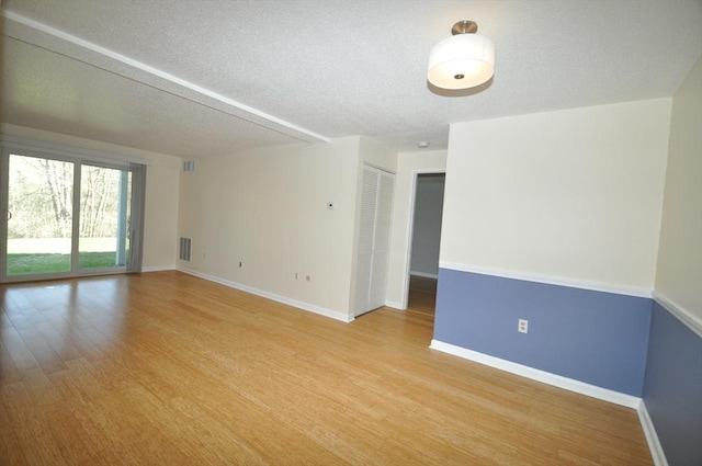 spare room with light wood-style floors, a textured ceiling, baseboards, and visible vents