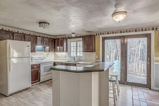 kitchen with white appliances, sink, dark brown cabinets, kitchen peninsula, and a breakfast bar area