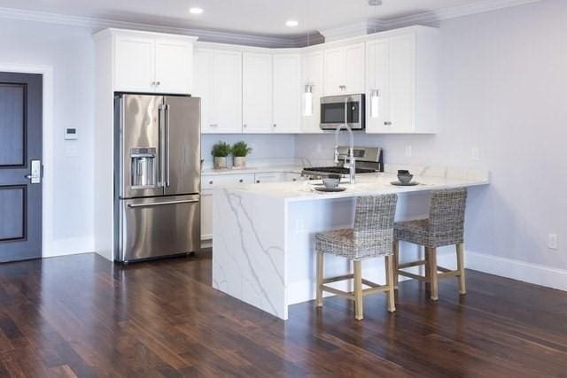 kitchen featuring a breakfast bar, white cabinets, ornamental molding, dark hardwood / wood-style flooring, and stainless steel appliances