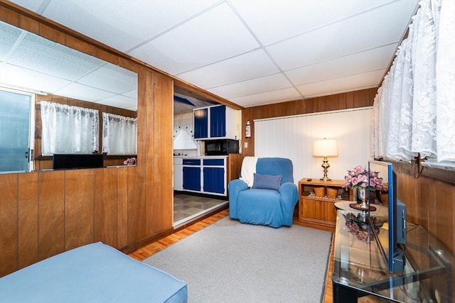 living area with hardwood / wood-style flooring, a drop ceiling, and wood walls