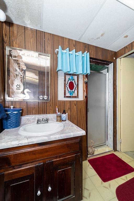 bathroom featuring wood walls, lofted ceiling, vanity, a shower with door, and a textured ceiling