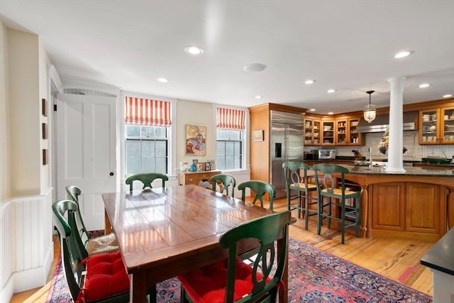 dining area featuring light wood finished floors, recessed lighting, bar area, and decorative columns