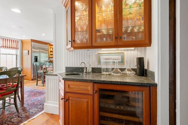 bar with light wood-style flooring, stainless steel built in refrigerator, a sink, wine cooler, and wet bar