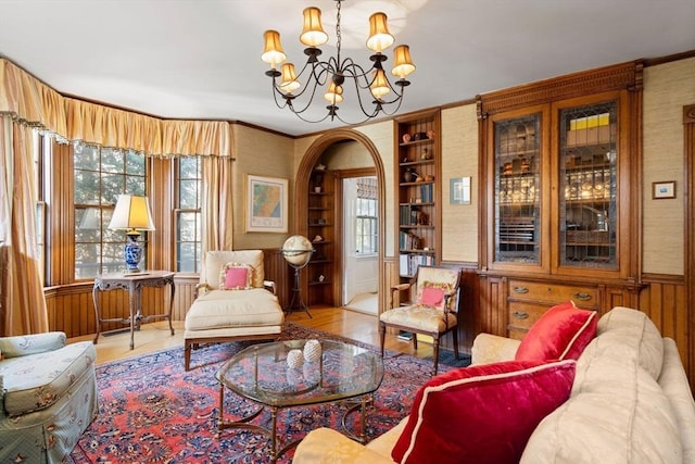 sitting room with built in shelves, wood finished floors, arched walkways, an inviting chandelier, and wainscoting