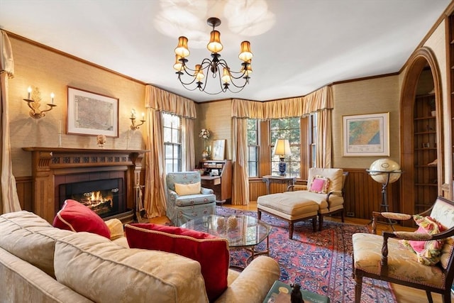 sitting room featuring wallpapered walls, a chandelier, a lit fireplace, ornamental molding, and wood finished floors