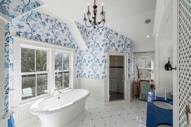 bathroom with a freestanding tub, a sink, wallpapered walls, a shower stall, and wainscoting