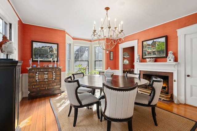 dining space featuring a fireplace with flush hearth, light wood-type flooring, crown molding, and an inviting chandelier