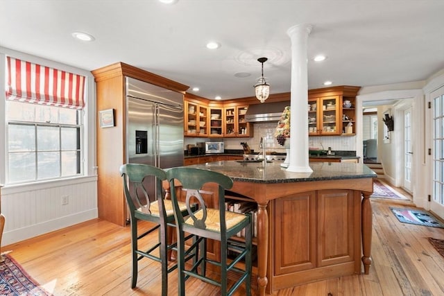 kitchen featuring built in refrigerator, light wood finished floors, brown cabinetry, and ornate columns