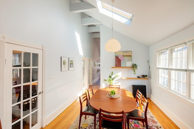 dining space featuring radiator heating unit, hardwood / wood-style flooring, high vaulted ceiling, and a skylight