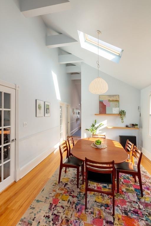 dining room featuring hardwood / wood-style flooring, lofted ceiling with skylight, and radiator