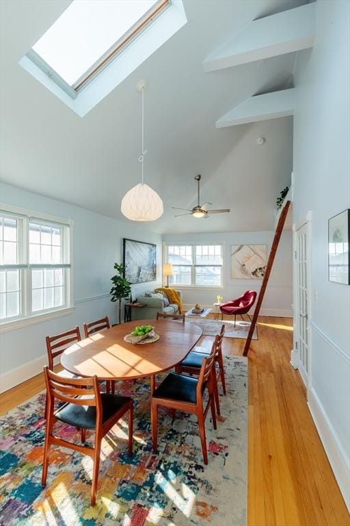 dining room featuring high vaulted ceiling, a skylight, beamed ceiling, and light wood-type flooring