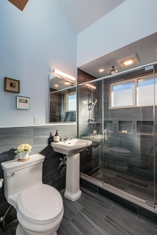 bathroom with toilet, a shower with shower door, and tile walls