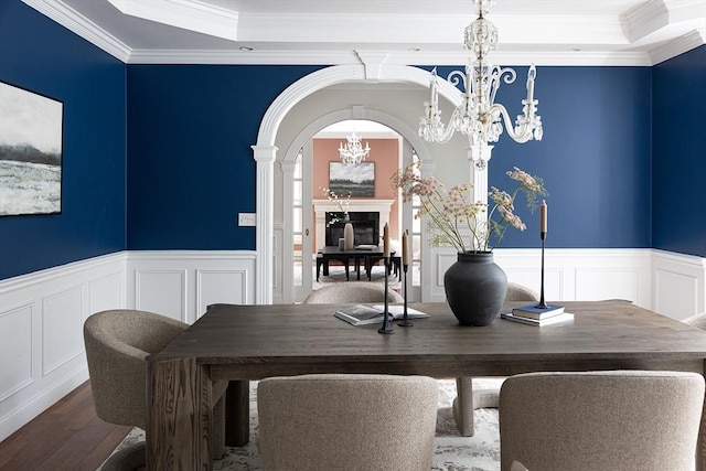 dining area with arched walkways, wainscoting, wood finished floors, and a notable chandelier