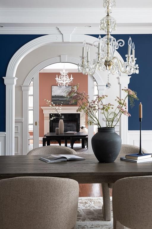 dining space with arched walkways, a wainscoted wall, wood finished floors, and decorative columns