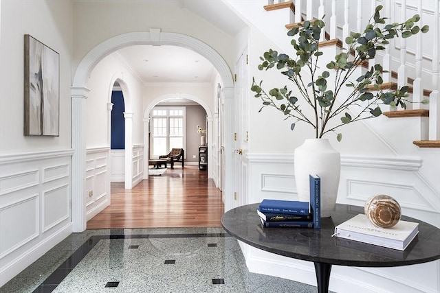 hall with arched walkways, wainscoting, ornamental molding, granite finish floor, and a decorative wall