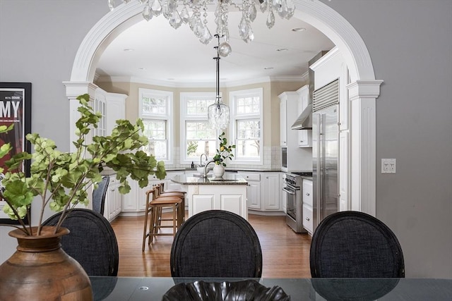 kitchen featuring light wood finished floors, white cabinets, premium appliances, wall chimney exhaust hood, and a kitchen island