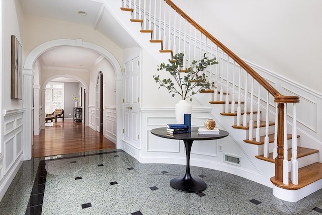 foyer entrance with arched walkways, a wainscoted wall, granite finish floor, and a decorative wall