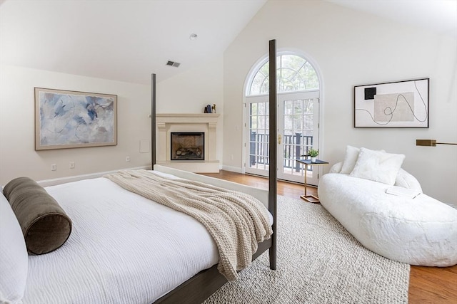 bedroom featuring a fireplace with raised hearth, high vaulted ceiling, light wood-style flooring, visible vents, and access to exterior