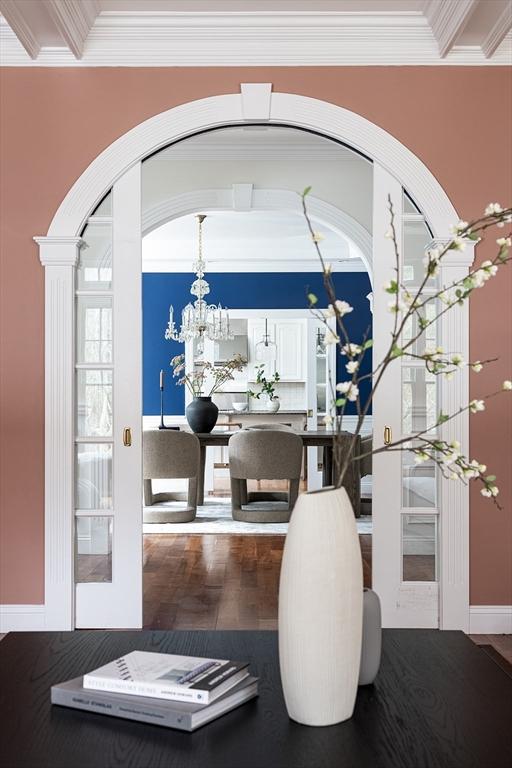 interior space featuring arched walkways, a notable chandelier, wood finished floors, french doors, and crown molding