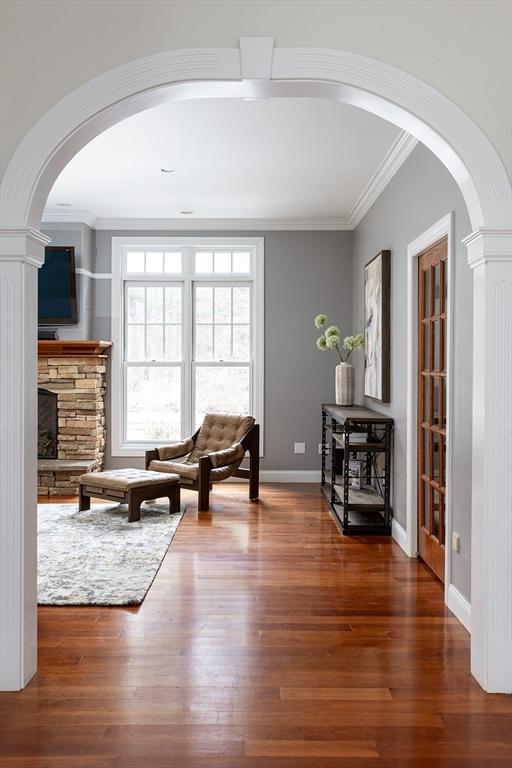 living area with arched walkways, a stone fireplace, wood finished floors, baseboards, and ornamental molding