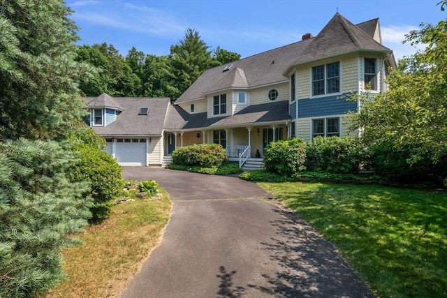 view of front of home featuring a garage, covered porch, driveway, and a front yard