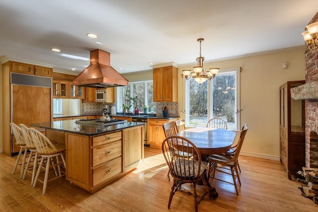 kitchen with island range hood, light wood-style flooring, stainless steel appliances, backsplash, and a chandelier