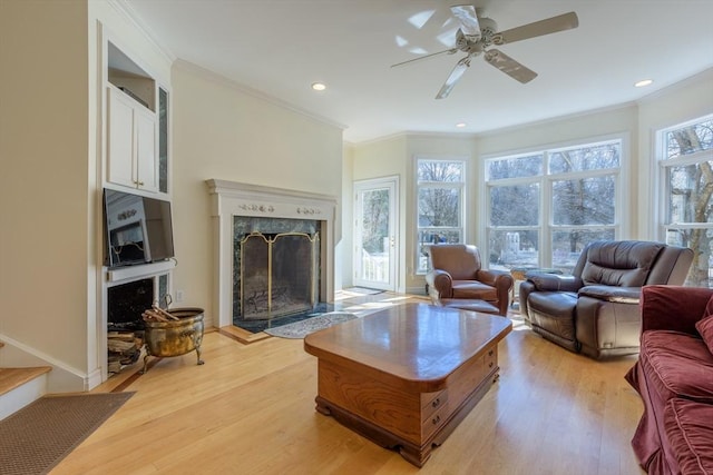 living area with light wood-type flooring, recessed lighting, crown molding, a premium fireplace, and ceiling fan