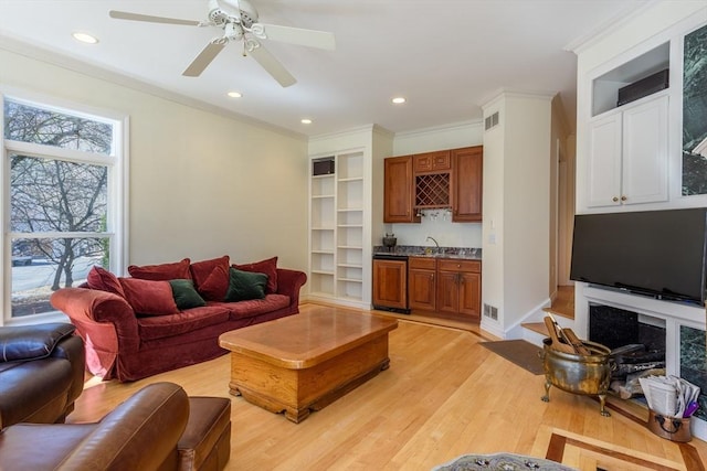 living room with visible vents, ornamental molding, indoor wet bar, recessed lighting, and light wood-style floors