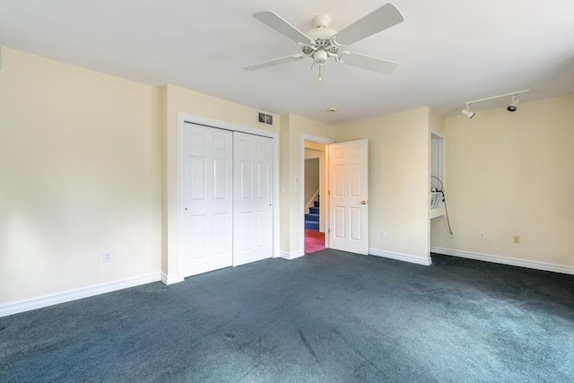 unfurnished bedroom featuring baseboards, visible vents, rail lighting, a closet, and dark carpet