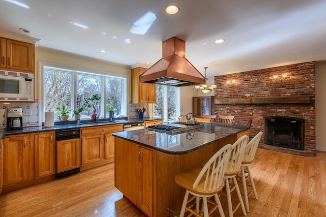 kitchen featuring brown cabinetry, island exhaust hood, stainless steel appliances, light wood-style floors, and a center island