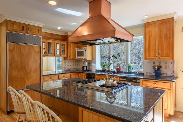 kitchen with paneled refrigerator, ornamental molding, island exhaust hood, a center island, and white microwave