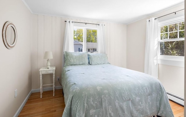 bedroom with baseboard heating, ornamental molding, multiple windows, and wood finished floors