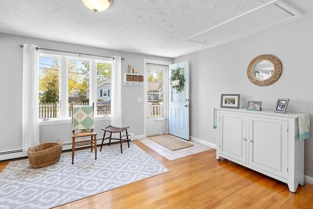 entrance foyer featuring a textured ceiling, a baseboard heating unit, and light wood-style flooring