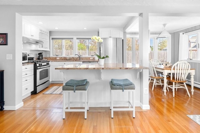 kitchen featuring a healthy amount of sunlight, a kitchen breakfast bar, white cabinets, under cabinet range hood, and stainless steel appliances
