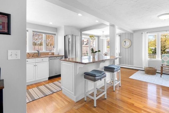 kitchen featuring white cabinets, a breakfast bar area, dark stone countertops, stainless steel appliances, and light wood-type flooring