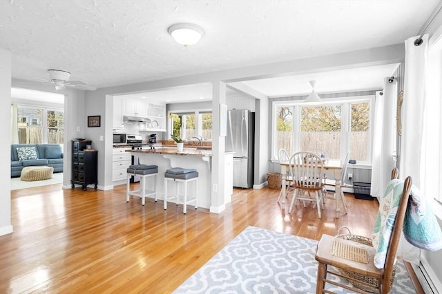 living room with a ceiling fan, a baseboard heating unit, a wealth of natural light, and light wood-type flooring