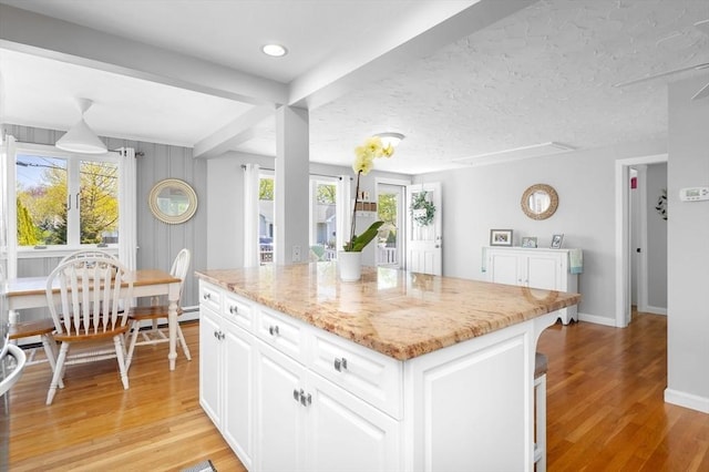 kitchen with light wood-style floors, baseboards, a center island, white cabinetry, and light stone counters