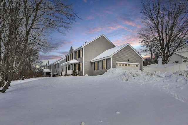 view of snow covered exterior featuring a garage and fence