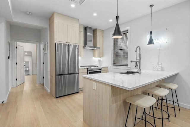 kitchen with wall chimney range hood, light wood-type flooring, decorative light fixtures, kitchen peninsula, and stainless steel appliances