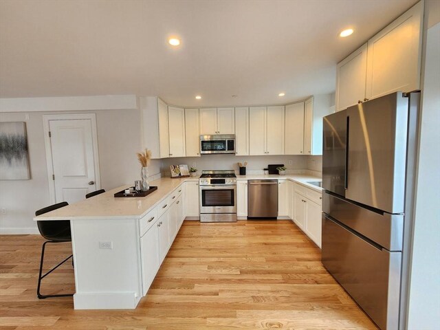 kitchen featuring white cabinets, light hardwood / wood-style floors, stainless steel appliances, and a breakfast bar area