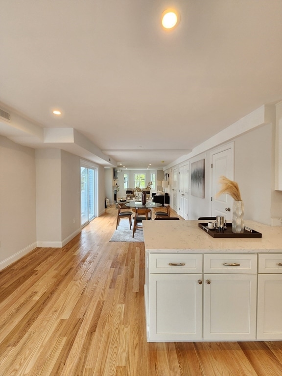 kitchen with light hardwood / wood-style floors, light stone counters, and white cabinetry