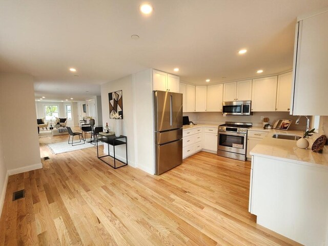 kitchen with white cabinets, stainless steel appliances, light hardwood / wood-style floors, and sink