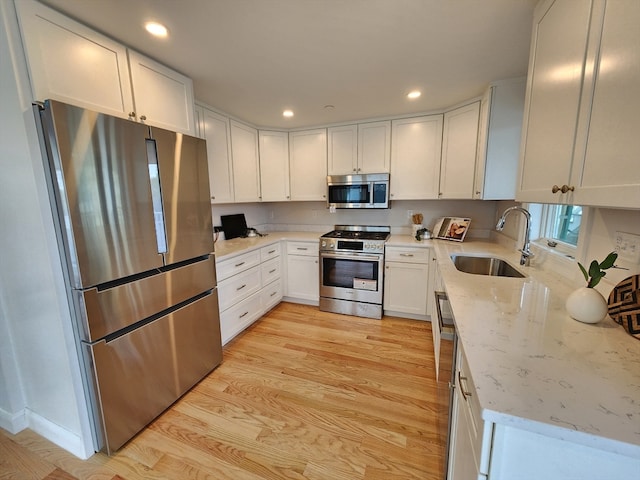 kitchen featuring light stone countertops, white cabinetry, sink, appliances with stainless steel finishes, and light wood-type flooring