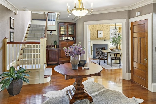 entryway featuring hardwood / wood-style flooring, a fireplace, crown molding, a chandelier, and stairs