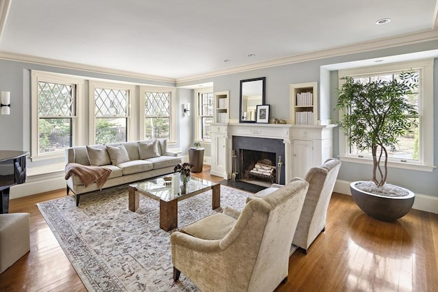 living area featuring baseboards, a fireplace with flush hearth, wood finished floors, and crown molding