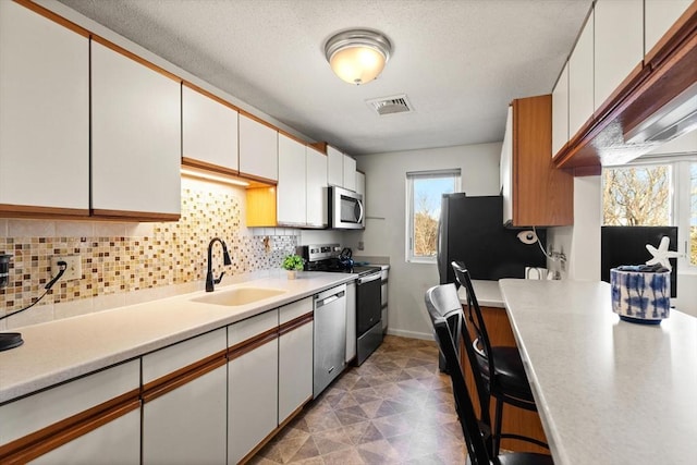 kitchen with stainless steel appliances, tasteful backsplash, sink, and white cabinets