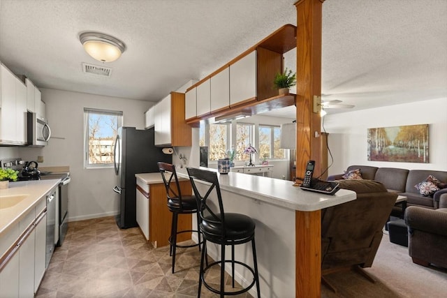 kitchen featuring a kitchen breakfast bar, kitchen peninsula, white cabinets, and appliances with stainless steel finishes